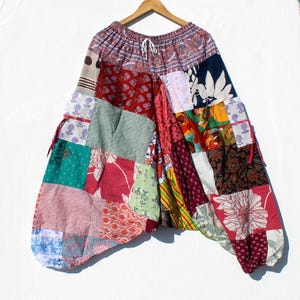 以下が含まれることがあります： 様々な色と柄のパッチワークハーレムパンツ。花柄、ペイズリー柄、幾何学模様など。パンツはドローストリングウエストで、木製のハンガーに吊るされています。