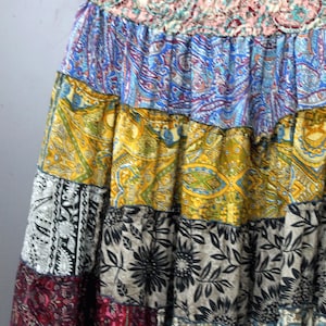 May include: A patchwork skirt with a gathered waistband. The skirt features panels of various patterned fabrics in shades of blue, yellow, black, and red. The patterns include paisley, floral, and geometric designs, creating a bohemian aesthetic.