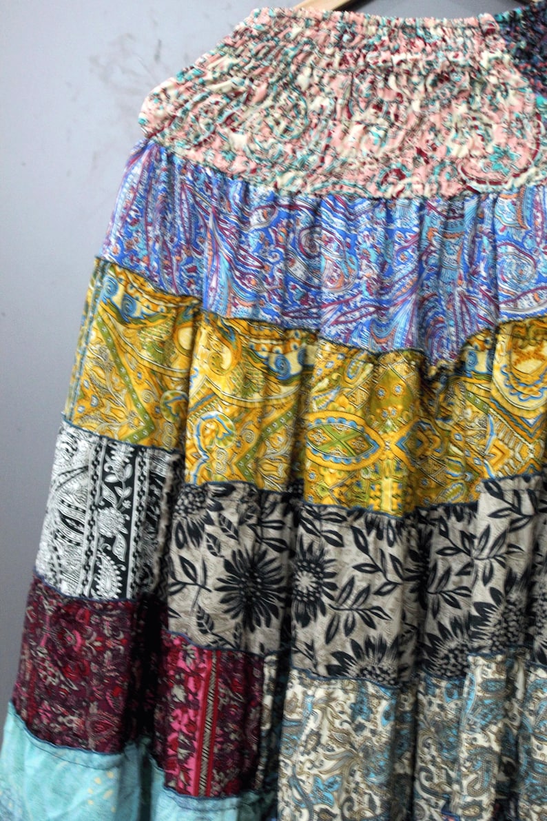 May include: A patchwork skirt with a gathered waistband. The skirt features panels of various patterned fabrics in shades of blue, yellow, black, and red. The patterns include paisley, floral, and geometric designs, creating a bohemian aesthetic.