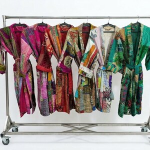 May include: Six long-sleeved robes with tie belts hanging on a metal rolling rack. Each robe features a unique patchwork design with intricate stitching and a variety of vibrant colors including pink, red, orange, yellow, blue, and green.