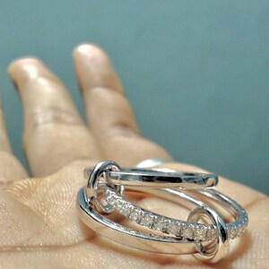 Pu&ograve; includere: Un anello color argento dal design multistrato composto da tre fasce circolari interconnesse. Una delle fasce &egrave; incastonata con una fila di piccole pietre chiare e scintillanti, mentre le altre due fasce sono lisce e lucide.