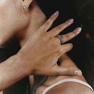 Pu&ograve; includere: Un orecchino a lobo circolare color argento con un piccolo cerchio pendente e un anello a pi&ugrave; fasce con una fila centrale di pietre trasparenti. Il set di gioielli &egrave; realizzato in metallo lucido con un design coerente e dettagliato.
