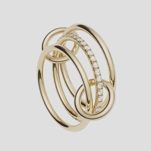 Pu&ograve; includere: Un anello a pi&ugrave; fasce realizzato in oro giallo lucido, caratterizzato da tre cerchi intrecciati. Una delle fasce &egrave; incastonata con una fila continua di piccoli diamanti bianchi rotondi e chiari che catturano la luce, creando un effetto a strati.