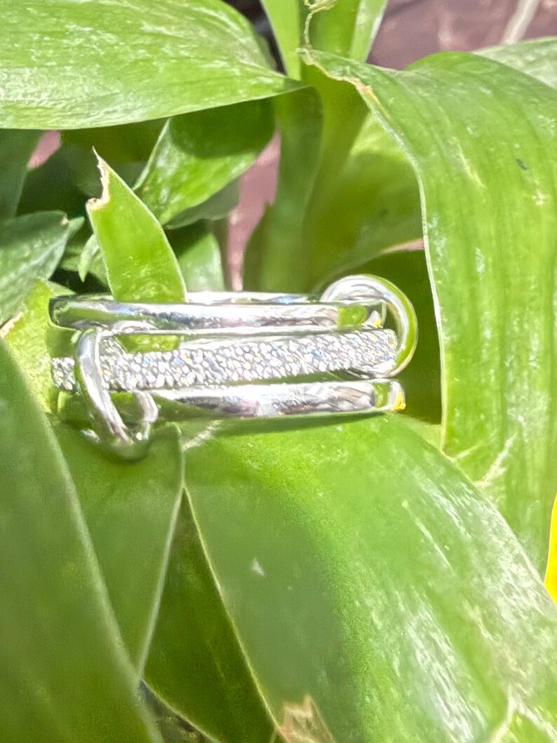 Pu&ograve; includere: Un anello multi-fascia color argento composto da una combinazione di fasce in metallo liscio e lucido e una fascia centrale con una finitura testurizzata e scintillante. Il design presenta diversi anelli intrecciati tra loro.