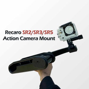 Op de afbeelding: Zwarte action camera mount met een heldere camera bevestigd. De mount is ontworpen voor Recaro SR2/SR3/SR5 modellen. De tekst "Recaro SR2/SR3/SR5 Action Camera Mount" wordt weergegeven. De mount wordt door een persoon vastgehouden.
