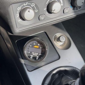 Może przedstawiać: Wnętrze samochodu z deską rozdzielczą i pokrętłami klimatyzacji. Widoczny jest wskaźnik AEM stosunku powietrza do paliwa. Czarna tarcza wyświetla cyfry i tekst "AIR/FUEL RATIO".