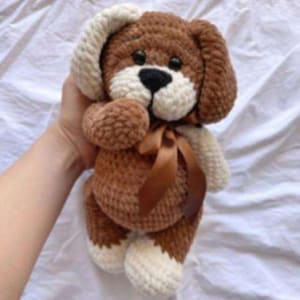 Puede incluir: Un peluche de perro hecho a mano con ganchillo, con detalles en marr&oacute;n y blanco. El perro tiene una nariz negra, un hocico blanco y una cinta marr&oacute;n. Perfecto para ni&ntilde;os.