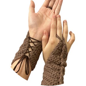 May include: Brown crochet wrist cuffs with a lace-up design. The cuffs are fingerless and made of a textured, woven material. The lace-up detail is visible on the wrist, with the ties hanging down. The cuffs are shown on a person's hands.