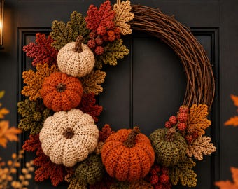 May include: A circular wreath constructed from brown twigs, decorated with crocheted pumpkins in cream and orange, alongside crocheted autumn leaves in shades of red, olive green, and tan, plus small clusters of red crocheted berries.