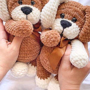Peut inclure: Deux peluches de chien faites à la main au crochet. Les chiens sont bruns avec des accents blancs sur les oreilles, les pattes et le museau. Chaque chien a un nez noir, des yeux foncés et un ruban marron autour du cou. Les jouets sont doux et moelleux.