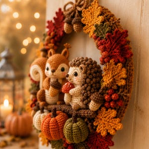 May include: A decorative autumn wreath crafted from crochet, featuring a brown squirrel holding an acorn and a hedgehog holding a mushroom. The wreath is adorned with crocheted orange, yellow, and red maple leaves, small pumpkins, and berries.