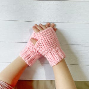 May include: A pair of light pink, fingerless crochet gloves. The gloves are made with a textured stitch and feature a ribbed cuff. The open-finger design allows for dexterity while keeping hands warm. Ideal for cooler weather.