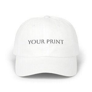Könnte beinhalten: Eine weiße Baseballkappe mit dem Text YOUR PRINT in schwarzen, serifenlosen Großbuchstaben, die mittig auf der Vorderseite platziert sind. Die Kappe hat eine strukturierte Krone, einen gebogenen Schirm und einen Knopf in der Mitte oben.