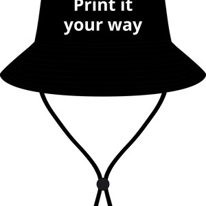 May include: A solid black bucket hat featuring a wide brim and a chin strap with an adjustable toggle. The front of the hat displays the white text "Print it your way" in a clean, sans-serif font, centered on the crown of the headwear.