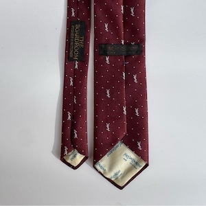 May include: A burgundy tie with a white polka dot pattern and small white logos. The tie has labels that read "THE BOARDROOM HUGHES & HATCHER" and "YVES SAINT LAURENT NEW YORK".