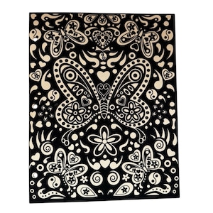 May include: Black and cream-colored decorative wooden panel featuring a symmetrical butterfly design. The butterfly and surrounding elements include hearts, flowers, and swirls. The design is a repeating pattern with a folk art style.