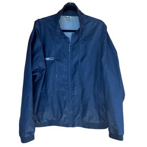 May include: A navy blue Puma jacket with a full-length zipper and a stand-up collar. The jacket has a white Puma logo on the left chest. The jacket is hanging on a black hanger.