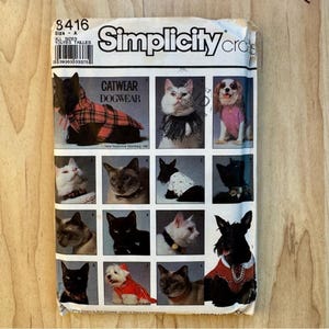 Puede incluir: Un sobre de patrón de costura Simplicity número 8416 para ropa de gatos y perros. El paquete de papel blanco presenta varias fotografías de gatos y perros vistiendo diversas prendas hechas a mano, incluyendo abrigos a cuadros y suéteres.