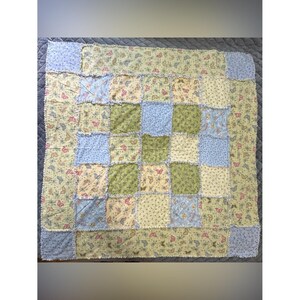May include: A square rag quilt featuring a patchwork design of alternating fabric squares in shades of light blue, sage green, and cream. The fabric is decorated with a repeating pattern of small butterflies and floral motifs with frayed edges.