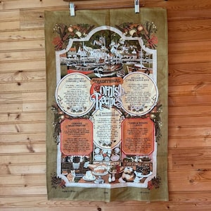 May include: A rectangular, olive-green cotton tea towel featuring traditional Cornish recipes. The towel includes illustrations of boats, food, and text. The text includes recipes for Cornish Mead, Meat Pasties, and Leek & Potato Soup.
