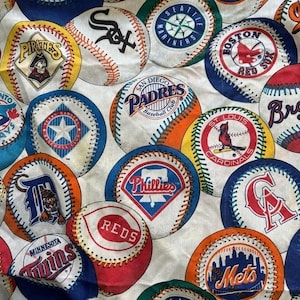 May include: A white fabric featuring a repeating pattern of various Major League Baseball team logos printed on baseballs. The design includes logos for the Pirates, White Sox, Mariners, Red Sox, Rangers, Padres, Cardinals, Tigers, Phillies, Reds, Twins, Mets, and Angels.