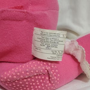 K&ouml;nnte beinhalten: Nahaufnahme eines rosa Pl&uuml;schtiers mit einem Etikett, das "NEUES MATERIAL NUR" angibt. Der Fu&szlig; des Spielzeugs hat ein strukturiertes, gepunktetes Muster. Hergestellt in China.