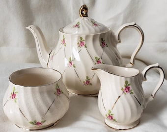 Juego de té vintage inglés con rosas: tetera, jarro para leche y azucarero, rosas rosas y detalles dorados, decoración estilo chintz cottagecore.
