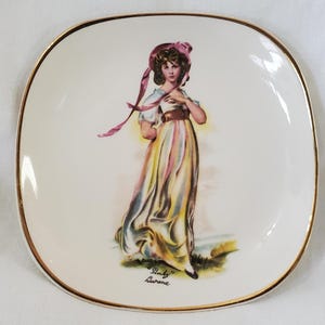 May include: Square porcelain plate with a gold rim. It features a colourful illustration of a woman in a long dress and a pink bonnet. The plate has the text "Pinky" Lawrence.