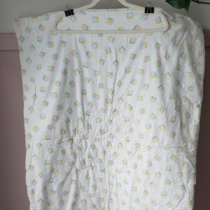 May include: White baby blanket with a repeating pattern of colorful letter blocks. The blocks feature the letters A, B, and C in pastel colors. The blanket is hanging on a white hanger.