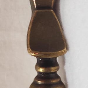 May include: An antique brass keyhole cover with a keyhole shape. The cover has an ornate design and a vintage aesthetic. It is likely used for furniture or decorative purposes.