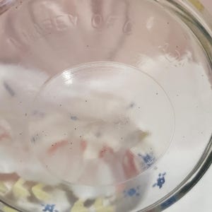 K&ouml;nnte beinhalten: Ein klares Glasgef&auml;&szlig; mit rundem Boden und leicht strukturierter Oberfl&auml;che. Das Gef&auml;&szlig; hat eine weite &Ouml;ffnung und ein klares, transparentes Aussehen. Auf dem Boden des Glases befindet sich schwer lesbarer Text. Das Glas steht auf einer wei&szlig;en Oberfl&auml;che.