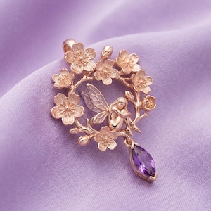 Peut inclure: Pendentif en or rose représentant une fée dans une couronne florale. Le pendentif comprend une pierre précieuse d'améthyste violette en forme de goutte. Le fond est un tissu lavande clair.