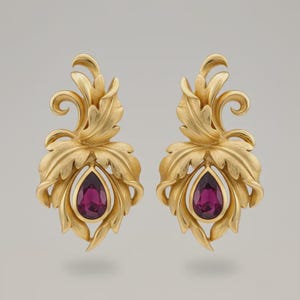 May include: A pair of gold-colored earrings with a leaf design. Each earring features a teardrop-shaped, deep purple gemstone. The earrings have an ornate, detailed design with a polished finish.