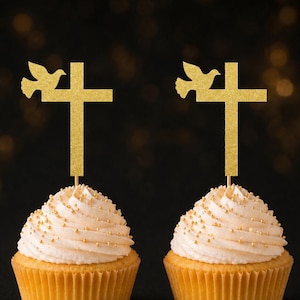 May include: Two cupcakes topped with gold glitter cross and dove cake toppers. Each cupcake features light-colored frosting decorated with small gold sprinkles, held in a light-colored paper liner, with a thin wooden pick supporting the topper.