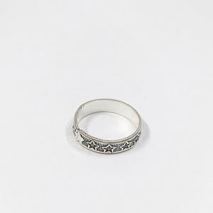 Könnte beinhalten: Ein silberner Ring mit einem sich wiederholenden Sternmuster um das Band. Der Ring ist vor einem weißen Hintergrund platziert, der das detaillierte Design hervorhebt. Der Ring scheint aus Metall zu sein.