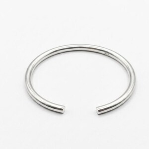 May include: A silver-colored open cuff bracelet. The bracelet is a simple, round band with a small gap. The metal has a shiny finish. The bracelet is marked with "925".