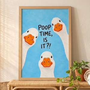 May include: A framed wall art print featuring three white geese with orange beaks against a light blue background. The text "POOP TIME, IS IT?!" is printed in black in the center. The frame is made of light-colored wood with a simple design.