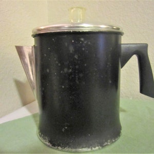 May include: A black metal percolator coffee pot with a silver lid and handle. The pot has a worn, speckled appearance.