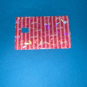 May include: A rectangular card with a red and white striped pattern, featuring the text "XOXO" and small heart shapes. The card has a rectangular cutout and holographic accents, set against a blue background.