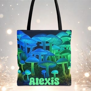 May include: A black tote bag featuring a vibrant illustration of glowing blue and green mushrooms. The word "Alexis" is written in green at the bottom. The bag has black handles.