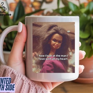 May include: A white ceramic mug featuring a doll image with the text "how I look at the man I love with all my heart." The mug has a white handle and the words "PRINTED BOTH SIDE" are printed on the side.
