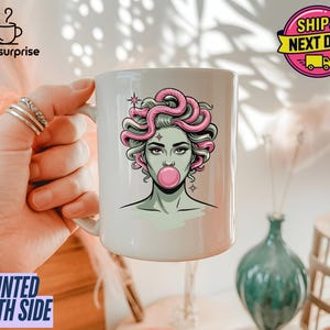 Può includere: Tazza in ceramica bianca con un'illustrazione ispirata a Medusa, con capelli rosa, pelle verde e una bolla di gomma da masticare. La tazza presenta il testo "magsurprise" e "PRINTED BOTH SIDE".
