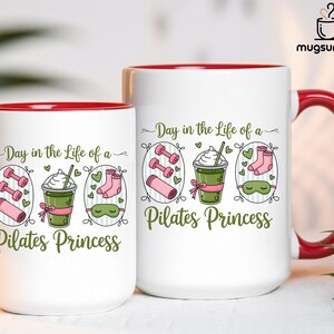 May include: Two white ceramic mugs with red interiors and handles. The mugs feature the text "Day in the Life of a Pilates Princess" with illustrations of dumbbells, a drink, socks, and a sleep mask. The mugs are for beverages.