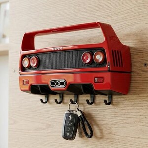 May include: A red wall-mounted key holder shaped like the rear of a Ferrari F40 sports car. It features a black mesh grille, four circular taillights, a central triple exhaust pipe, and five black metal hooks. A black car key fob hangs from one hook.
