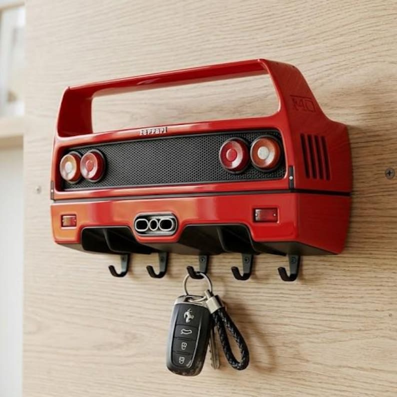 May include: A red wall-mounted key holder shaped like the rear of a Ferrari F40 sports car. It features a black mesh grille, four circular taillights, a central triple exhaust pipe, and five black metal hooks. A black car key fob hangs from one hook.