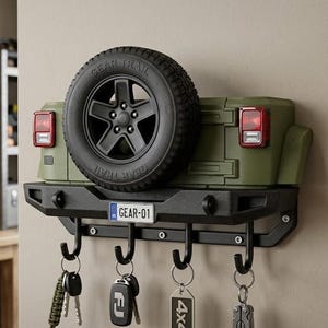 May include: A wall-mounted key holder designed like the rear of an olive green off-road vehicle. It features a black spare tyre, red taillights, a black bumper, and a number plate reading GEAR-01. Four black metal hooks hang below for keys.