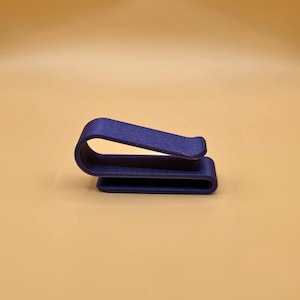 May include: A navy blue, curved metal clip. The clip has a rectangular base and a curved top section, creating a loop. The object is set against a light orange background.