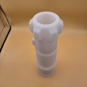 Pu&ograve; includere: Un raccordo idraulico in plastica bianca con un corpo cilindrico e una parte superiore svasata. Il raccordo ha una serie di creste e una base filettata. La parte superiore ha una serie di sporgenze. L'oggetto &egrave; posto su uno sfondo marrone chiaro.