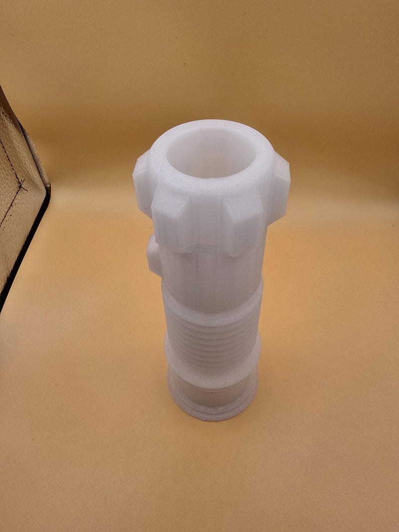 Pu&ograve; includere: Un raccordo idraulico in plastica bianca con un corpo cilindrico e una parte superiore svasata. Il raccordo ha una serie di creste e una base filettata. La parte superiore ha una serie di sporgenze. L'oggetto &egrave; posto su uno sfondo marrone chiaro.