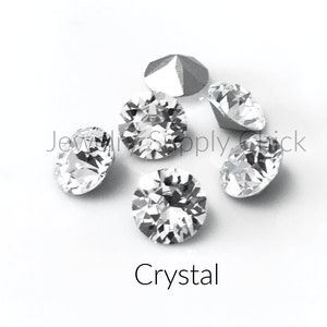 May include: A group of six clear crystal rhinestones on a white background. The rhinestones are round and have a faceted design.